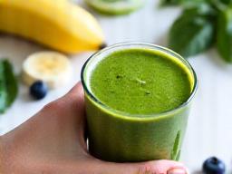 Hand holding a vibrant green smoothie with fresh ingredients, depicting healthy nutrition
