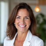 A friendly, professional female nutritionist smiling warmly, positioned against a clean, modern clinic or office backdrop.